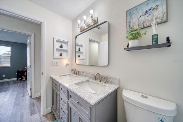 bathroom with double vanity, a sink, wood finished floors, and baseboards
