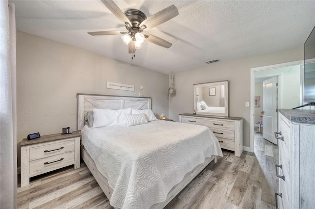 bedroom featuring a ceiling fan, visible vents, light wood-style flooring, and a textured ceiling
