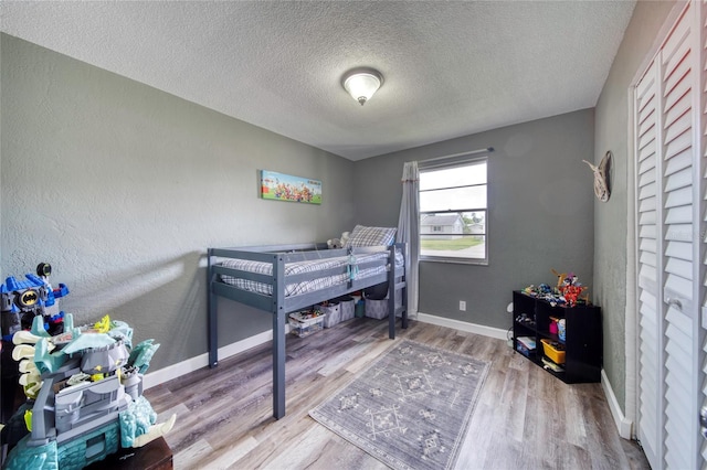 bedroom with baseboards, wood finished floors, a textured ceiling, and a textured wall