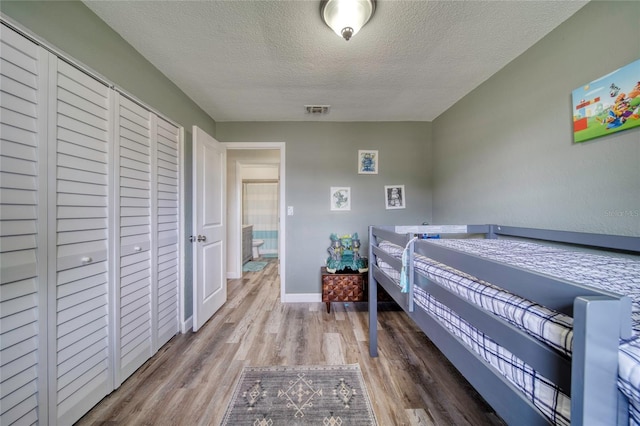 bedroom with baseboards, visible vents, wood finished floors, and a textured ceiling