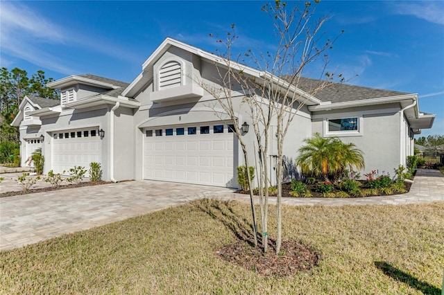 view of front facade featuring decorative driveway, roof with shingles, a front yard, an attached garage, and stucco siding