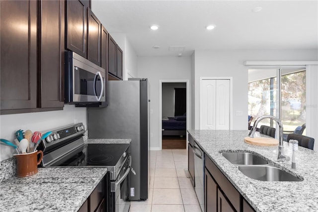 kitchen with dark brown cabinets, light tile patterned flooring, appliances with stainless steel finishes, light stone countertops, and a sink