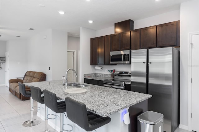 kitchen featuring dark brown cabinets, a breakfast bar area, light stone counters, a sink, and stainless steel appliances
