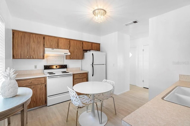 kitchen with under cabinet range hood, brown cabinetry, white appliances, and a notable chandelier
