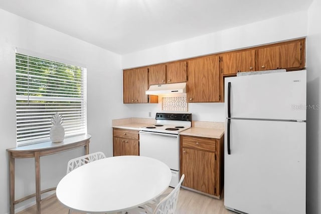 kitchen with white appliances, brown cabinets, under cabinet range hood, light wood-style flooring, and light countertops