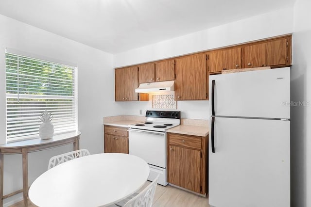 kitchen featuring under cabinet range hood, light countertops, brown cabinetry, and white appliances