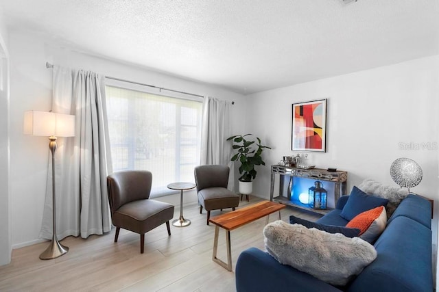 sitting room featuring baseboards, light wood-style floors, and a textured ceiling