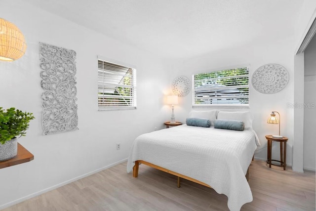 bedroom with multiple windows, wood finished floors, and baseboards