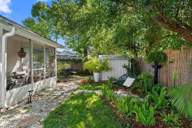 view of yard featuring a patio, a storage unit, a sunroom, a fenced backyard, and an outbuilding