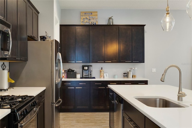 kitchen featuring hanging light fixtures, a sink, light wood-style floors, light countertops, and stainless steel appliances