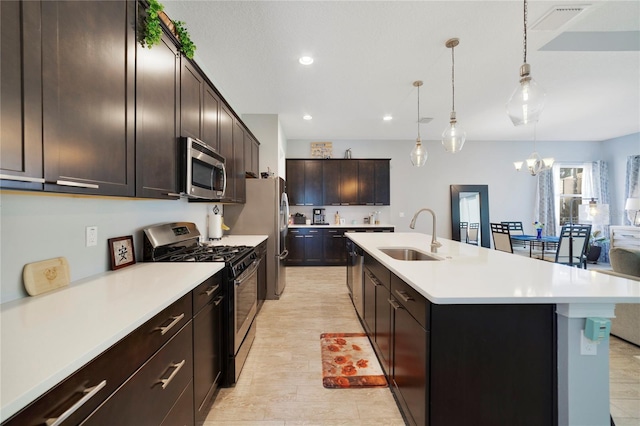kitchen featuring appliances with stainless steel finishes, a center island with sink, a sink, light countertops, and a notable chandelier