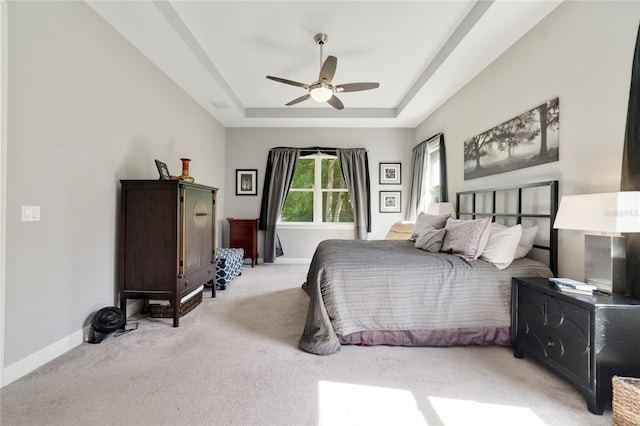 bedroom with a ceiling fan, a tray ceiling, light carpet, and baseboards