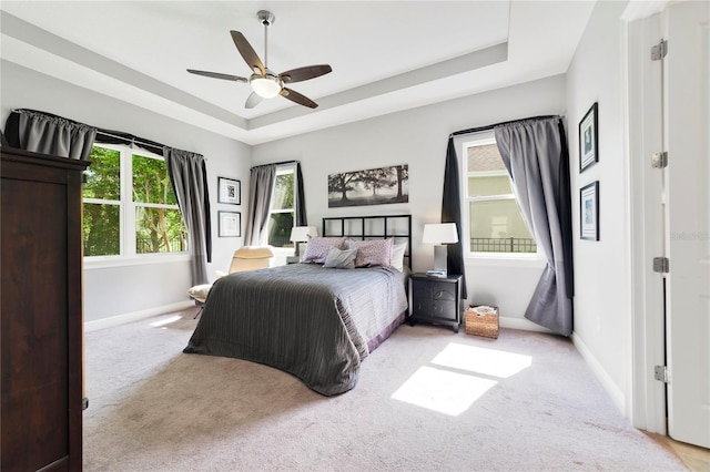 carpeted bedroom featuring baseboards, ceiling fan, and a tray ceiling