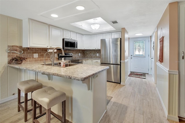 kitchen featuring a sink, a peninsula, stainless steel appliances, visible vents, and light countertops