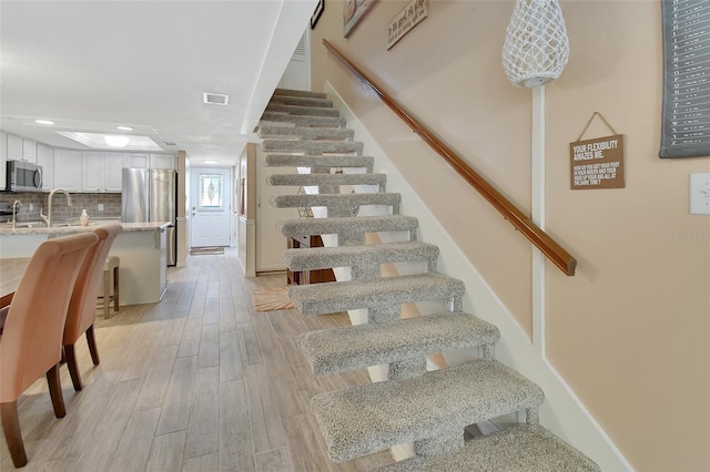 staircase featuring visible vents, wood finished floors, baseboards, and recessed lighting