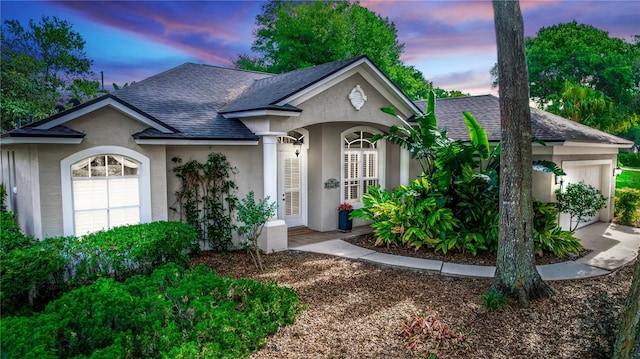 ranch-style home with a garage, roof with shingles, and stucco siding