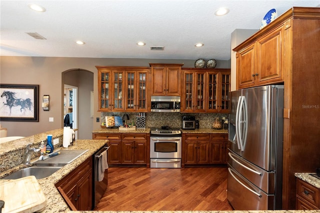 kitchen with a sink, arched walkways, stainless steel appliances, dark wood-type flooring, and visible vents