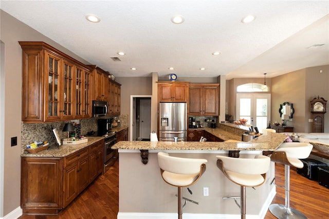kitchen featuring appliances with stainless steel finishes, light stone counters, dark wood-type flooring, and a kitchen bar