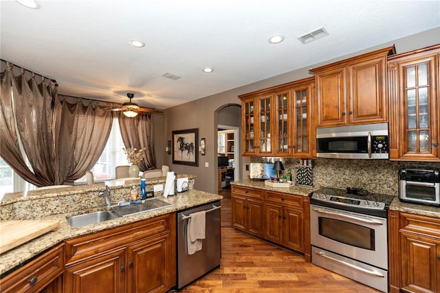 kitchen featuring appliances with stainless steel finishes, a sink, brown cabinetry, backsplash, and visible vents