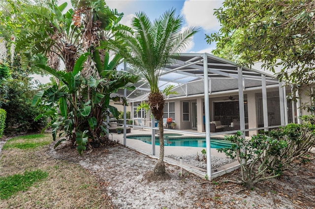 outdoor pool featuring glass enclosure, a patio, and a ceiling fan