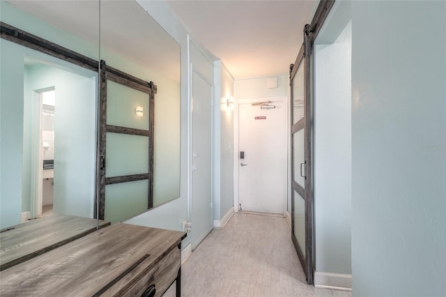 hallway featuring baseboards, a barn door, and light wood-style floors