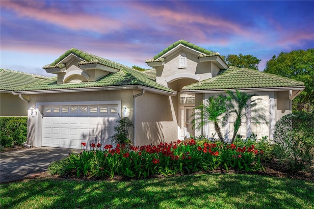 mediterranean / spanish house featuring an attached garage, stucco siding, driveway, and a tile roof