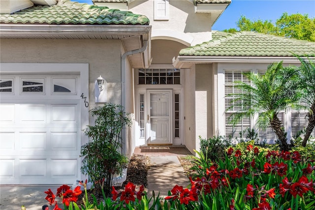 view of exterior entry with a tiled roof, an attached garage, and stucco siding