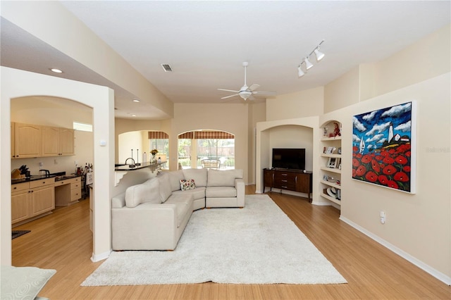 living area with baseboards, ceiling fan, built in shelves, and light wood-style flooring
