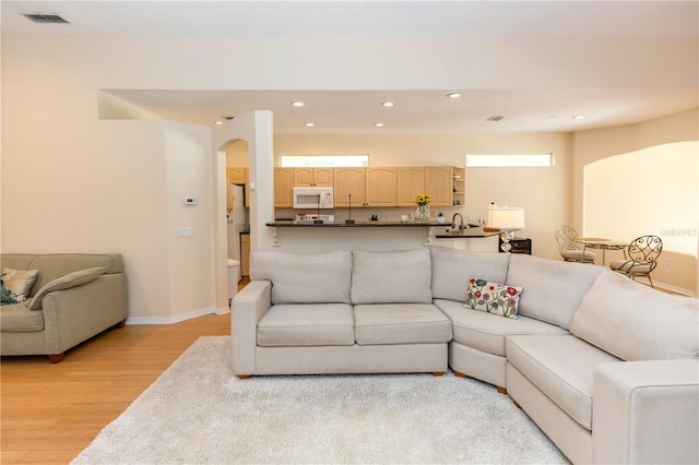 living area with visible vents, baseboards, recessed lighting, arched walkways, and light wood-style flooring