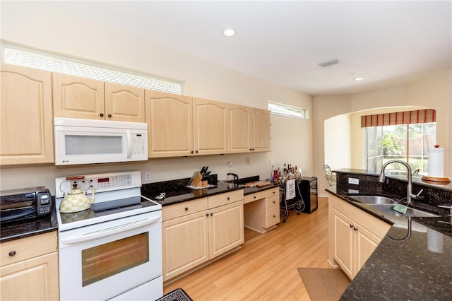 kitchen featuring light brown cabinetry, white appliances, dark stone countertops, a sink, and light wood finished floors