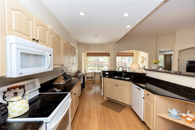 kitchen with arched walkways, a sink, light brown cabinets, white appliances, and light wood-style flooring