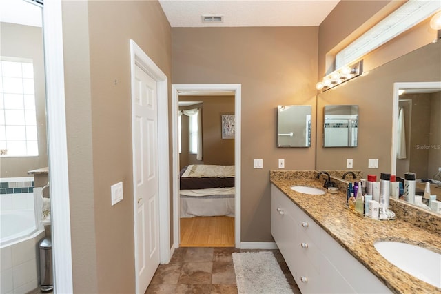 ensuite bathroom featuring baseboards, visible vents, a sink, and a garden tub