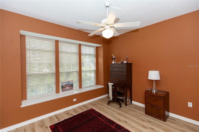 living area featuring a textured ceiling, baseboards, a ceiling fan, and wood finished floors