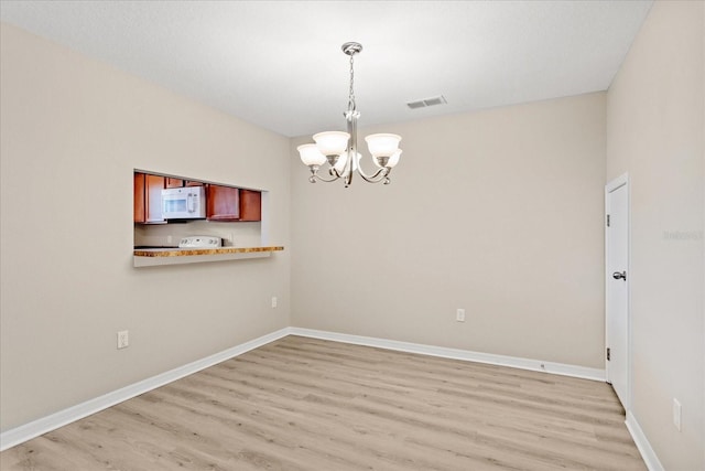 empty room featuring baseboards, a notable chandelier, visible vents, and light wood-type flooring