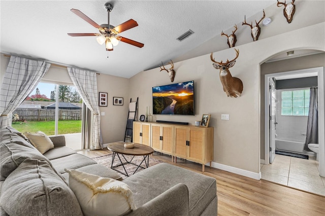 living room with visible vents, a ceiling fan, lofted ceiling, light wood-type flooring, and arched walkways