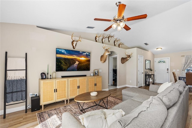 living area featuring ceiling fan, arched walkways, baseboards, wood finished floors, and vaulted ceiling