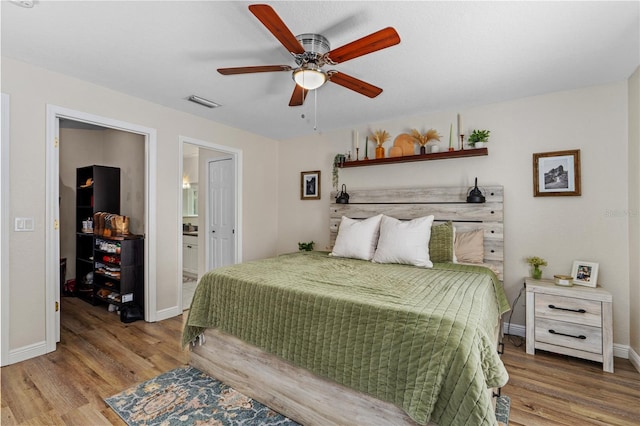 bedroom with baseboards, a ceiling fan, ensuite bath, and wood finished floors
