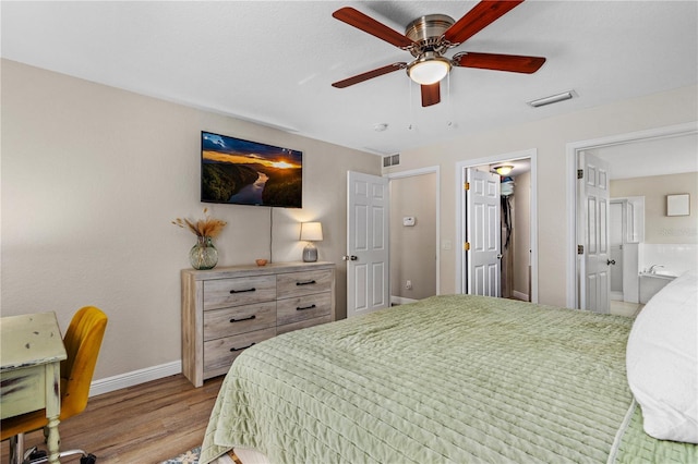 bedroom featuring visible vents, wood finished floors, baseboards, a ceiling fan, and ensuite bath