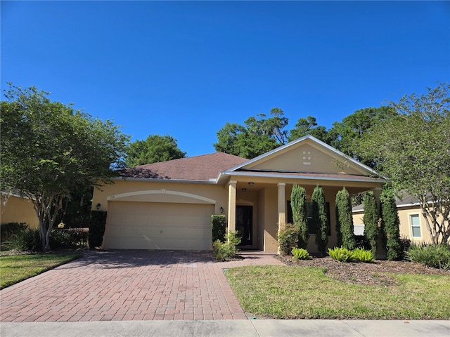 view of front of home featuring an attached garage, decorative driveway, stucco siding, and a front yard