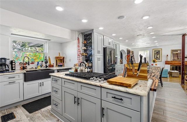 kitchen featuring a sink, stainless steel gas cooktop, light wood-type flooring, gray cabinetry, and high quality fridge