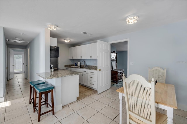 128 Oakridge Ave, Edgewater, FL 32132 - kitchen featuring a kitchen breakfast bar, visible vents, a sink, light tile patterned floors, and white cabinetry