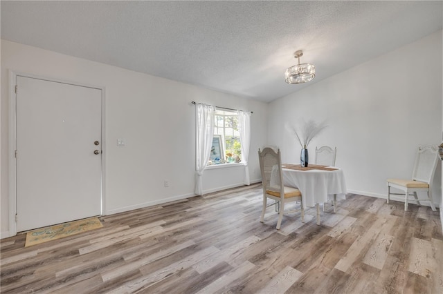 dining space with a textured ceiling, a notable chandelier, baseboards, and light wood finished floors