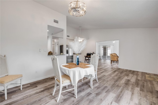 dining room featuring a chandelier, baseboards, lofted ceiling, light wood-type flooring, and visible vents