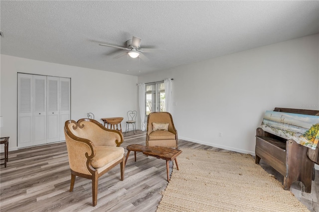 living area with baseboards, a textured ceiling, ceiling fan, and wood finished floors