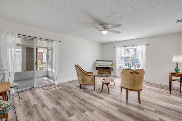 living area with visible vents, baseboards, a textured ceiling, a ceiling fan, and light wood finished floors