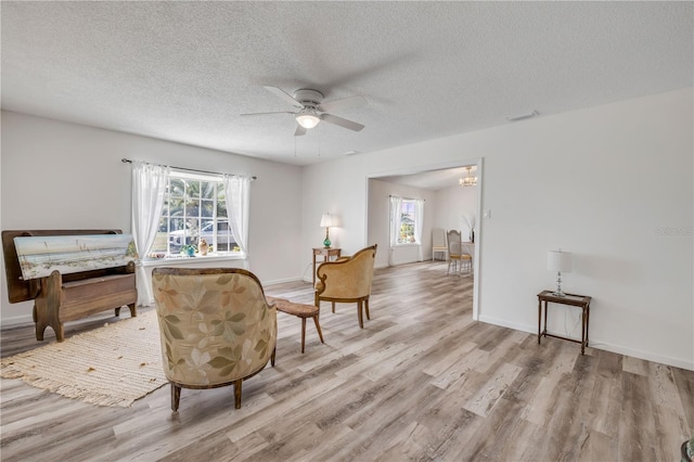 living area with light wood-style floors, a ceiling fan, a wealth of natural light, and visible vents