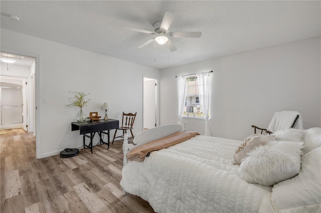 bedroom with a textured ceiling, attic access, a ceiling fan, baseboards, and wood finished floors