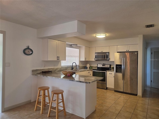kitchen featuring visible vents, a peninsula, white cabinets, dark stone countertops, and appliances with stainless steel finishes