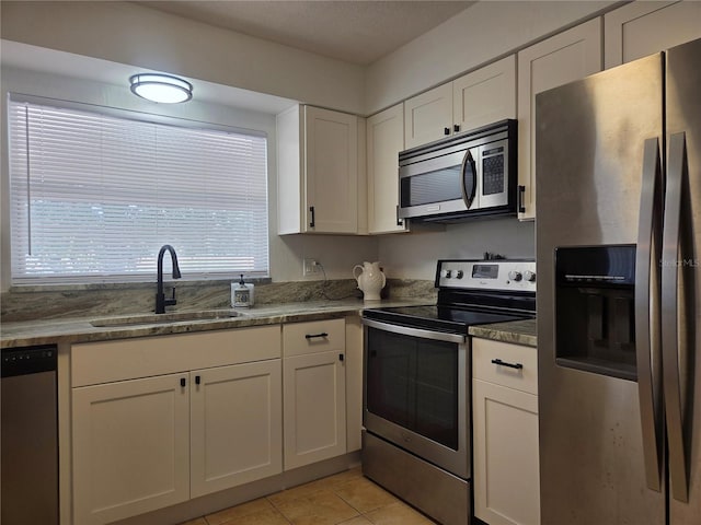 kitchen featuring light tile patterned flooring, appliances with stainless steel finishes, a sink, stone countertops, and white cabinetry