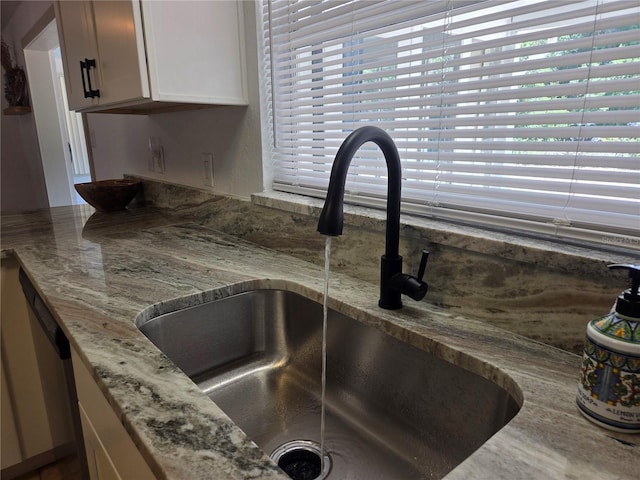 interior details with white cabinetry, light stone counters, a sink, and dishwasher